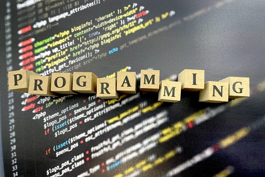 アルファベット１文字ずPROGRAMING
と書かれたブロックと、プログラムコードが書かれた板の写真