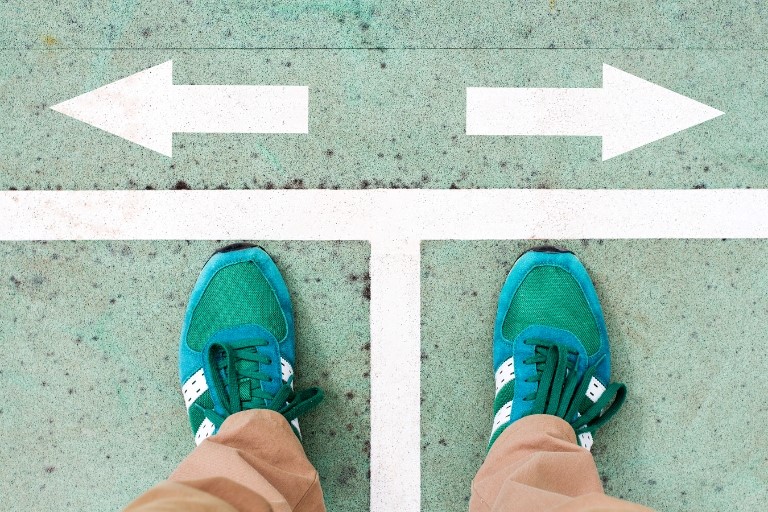 RPAエンジニアの主なキャリアパス3選のイメージ画像‐グリーンの靴を履いた男性の足元、白線をまたいでたっており、右矢印と左矢印のどちらに行くのかを考えているイメージ写真