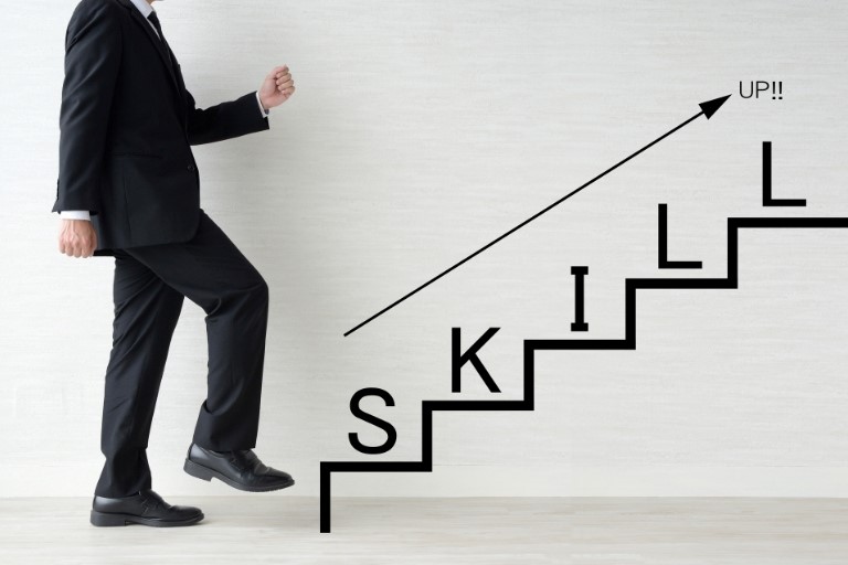 ネットワークエンジニアが将来性を高めるために習得すべきスキルのイメージ図‐スーツ姿の男性がSKILLと書かれた階段をのぼろうとしている様子