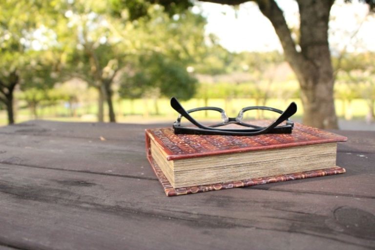 「文系出身の未経験者でも技術職として働ける理由」のイメージ画像‐公園の木の机の上に本と眼鏡が置かれている写真
