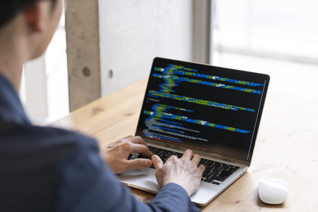 開発エンジニアとは？のイメージ写真‐ノートパソコンを操作しながらプログラミングを行っている男性の開発エンジニア。