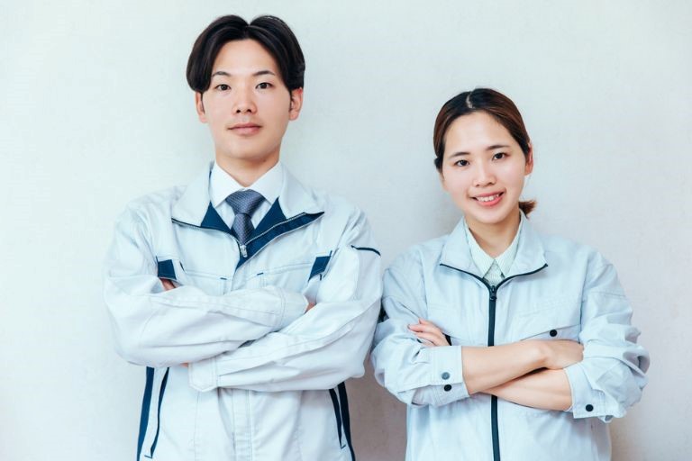 「製造業に向いている人の特徴7選」のイメージ画像‐製造業で働く作業服を着た２０代の男女が、自分の腕を組んでこちらを見ている。